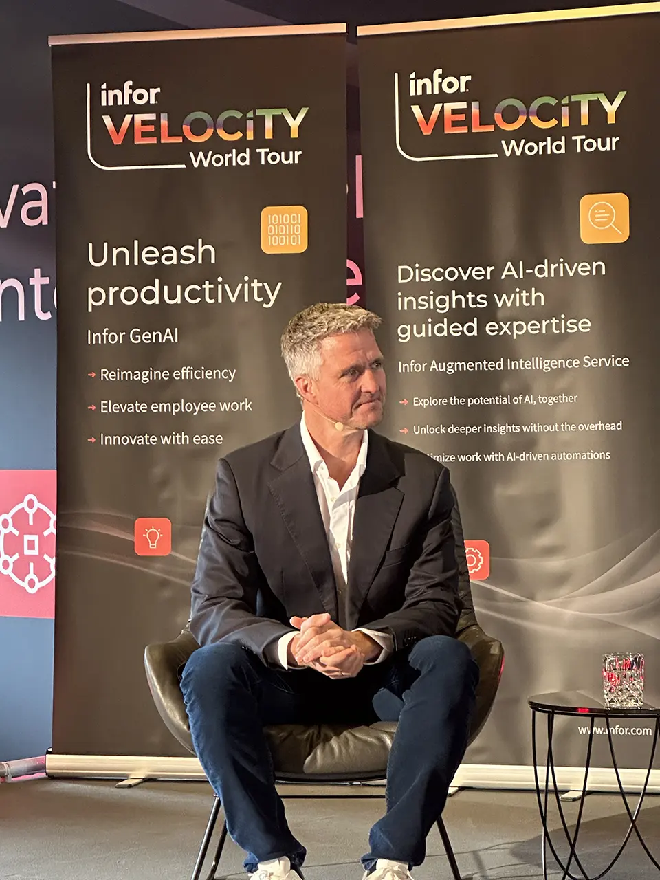 Ralf Schumacher sitzt auf einer Bühne als Keynote Speaker und hört aufmerksam zu