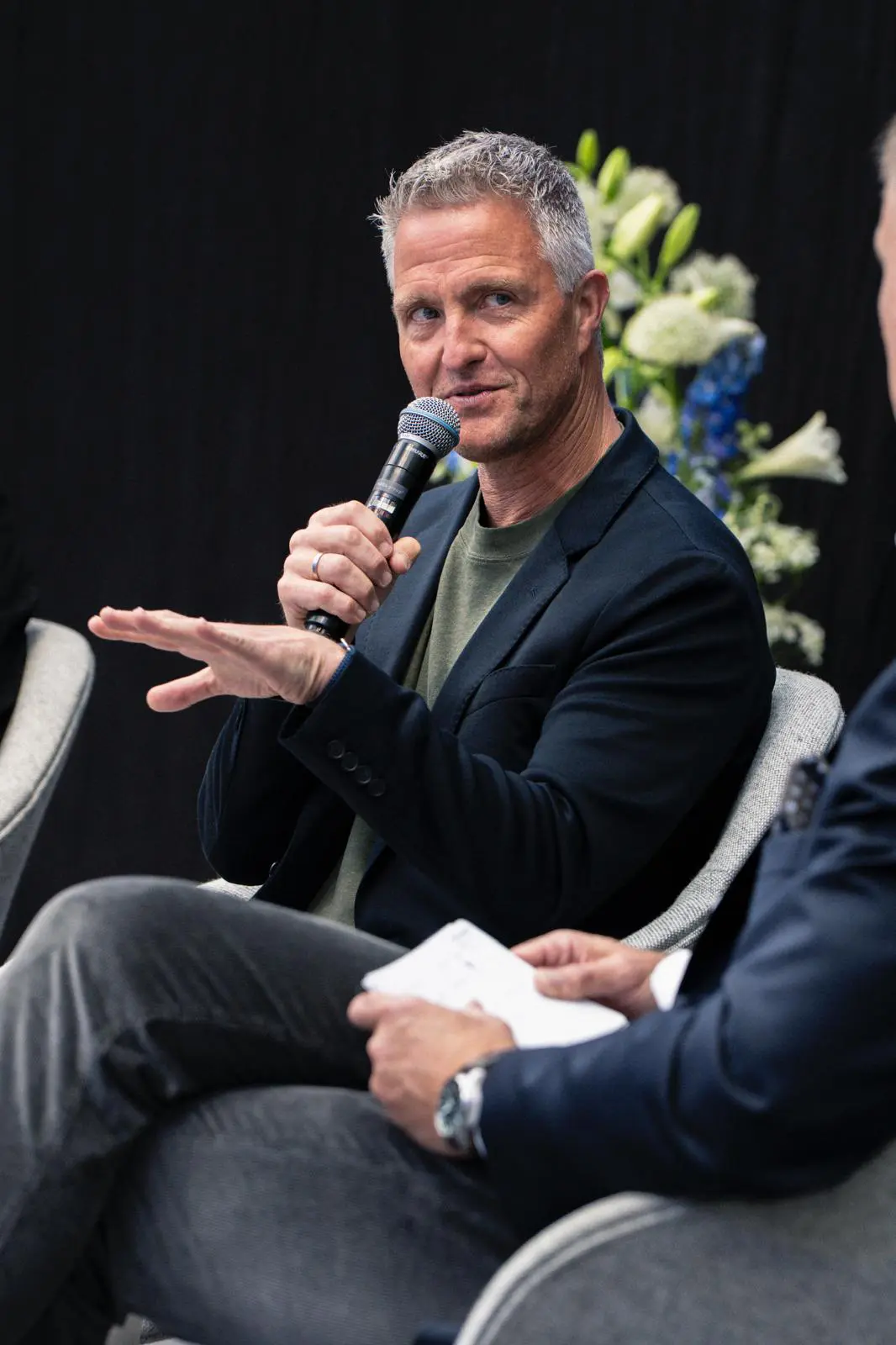 Ralf Schumacher spricht als Keynote Speaker im Bereich Motorsport in einer Podiumsdiskussion und hält ein Mikrofon