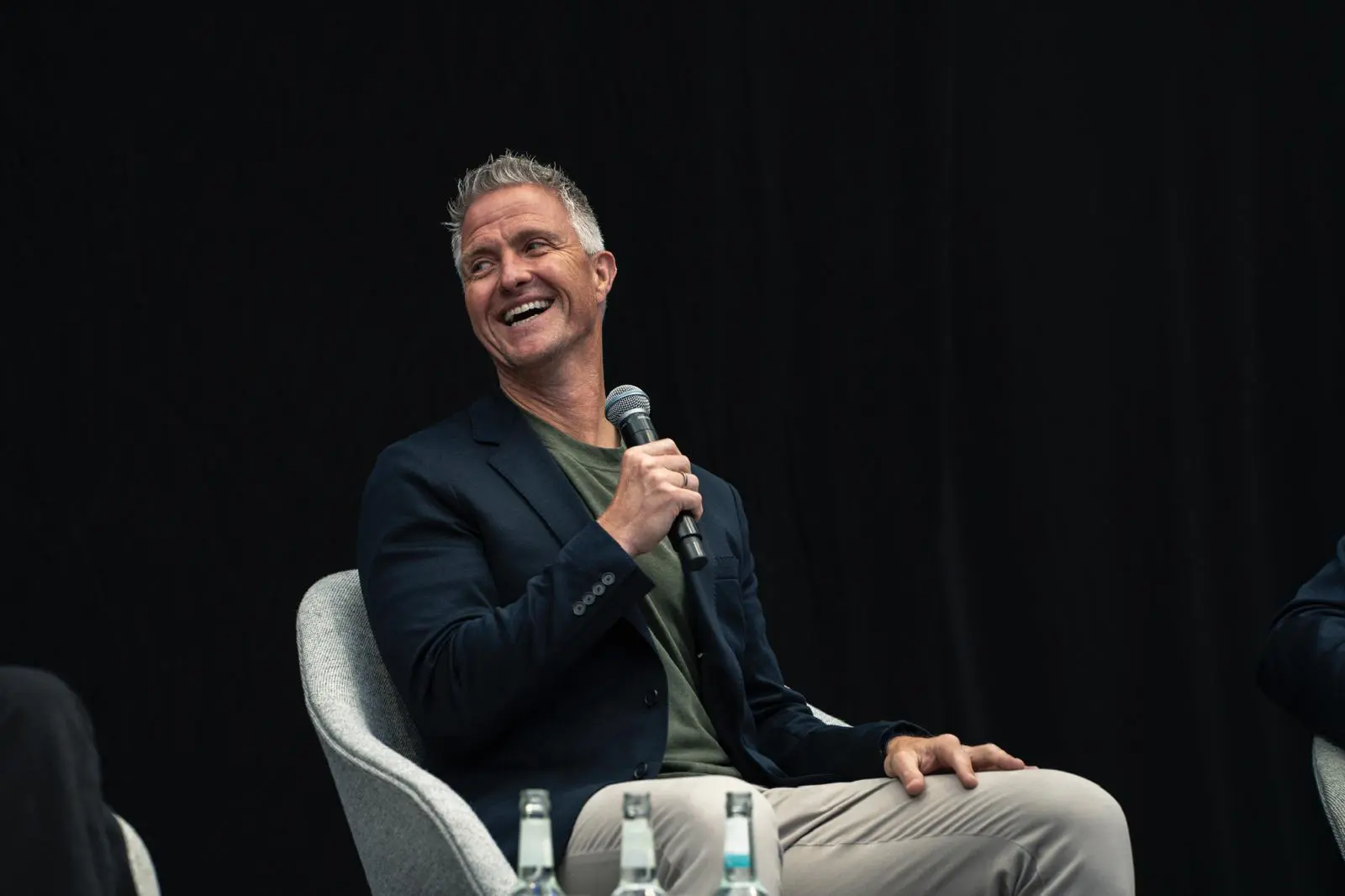 Ralf Schumacher lacht während seines Auftritts als Keynote Speaker und hält ein Mikrofon in der Hand